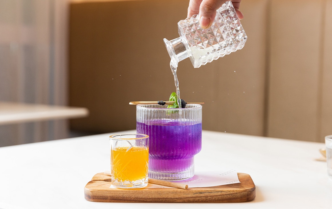a hand pouring a purple drink into a glass